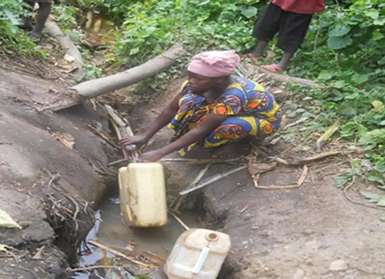 A woman collects water from an unprotected source, illustrating barriers to safe water access